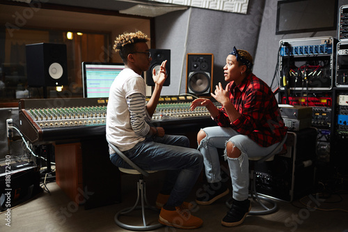 Two friendly African-american operators sitting in studio of records and discussing variants of mixing sounds