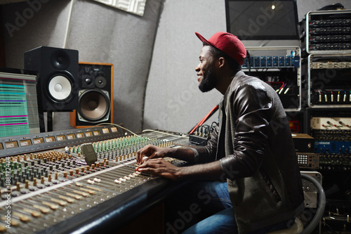 Happy young rapper sitting by recording equipment in audio production studio