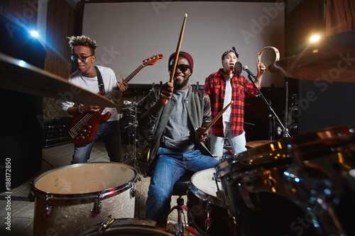 Band of young drummer, guitarist and singer playing instruments and performing songs in studio of records