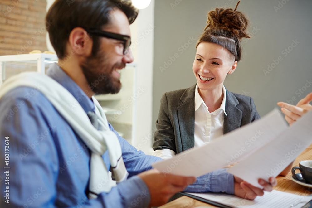 Happy female economist or banker and her colleague discussing papers or contracts Happy female economist or banker and her colleague discussing papers or contracts