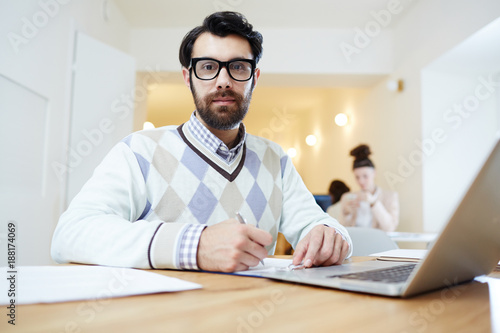 Young businassman in eyeglasses and smart casualwear looking at camera while preparing his report