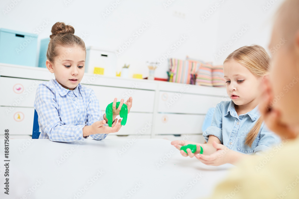 Fototapeta premium Little girls playing with green slime in kindergarten over table