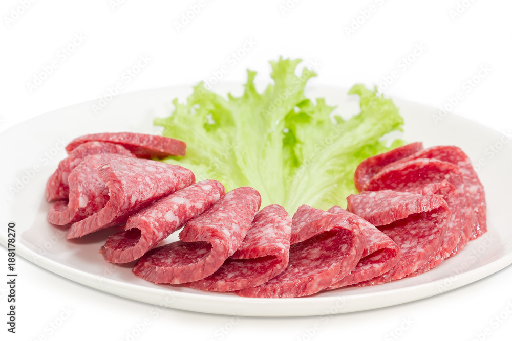 Sliced salami with lettuce leaf on a white dish closeup Sliced salami with lettuce leaf on a white dish closeup