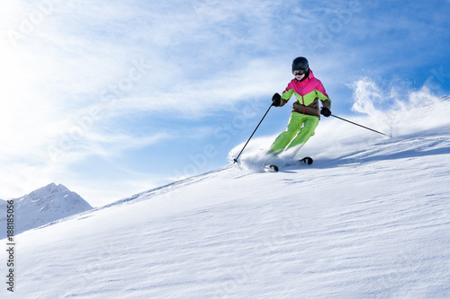 Junge sportliche Frau fährt Ski, macht Winter Sport in einem Winter Paradis. Schnee bedeckte Berge, blauer Himmel und Farbenfroher Ski Anzug