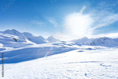 Junge sportliche Frau fährt Ski, macht Winter Sport in einem Winter Paradis. Schnee bedeckte Berge, blauer Himmel und Farbenfroher Ski Anzug © Merpics