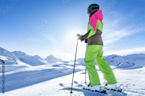 Junge sportliche Frau fährt Ski, macht Winter Sport in einem Winter Paradis. Schnee bedeckte Berge, blauer Himmel und Farbenfroher Ski Anzug