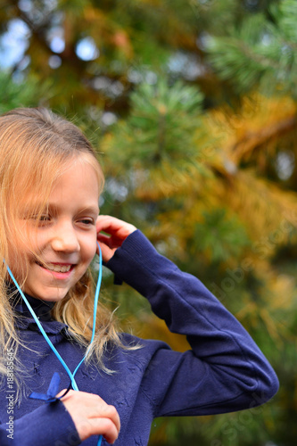 Happy young woman listening to music in forest. Young girl sitting on the stone in the autumn forest. Lonely girl with headphones. Beautiful girl wears headphones
