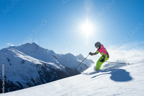 Young sexy woman is doing winter sport - she is skiing in a white winterparadis in the alps mountains. beautiful blue sky and snow powder  green dress  snow covered hills in winter