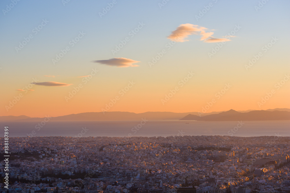 Aerial view of Athens (Greece), with Pireus port and Mediterranean Sea, with sunset sky and three clouds.