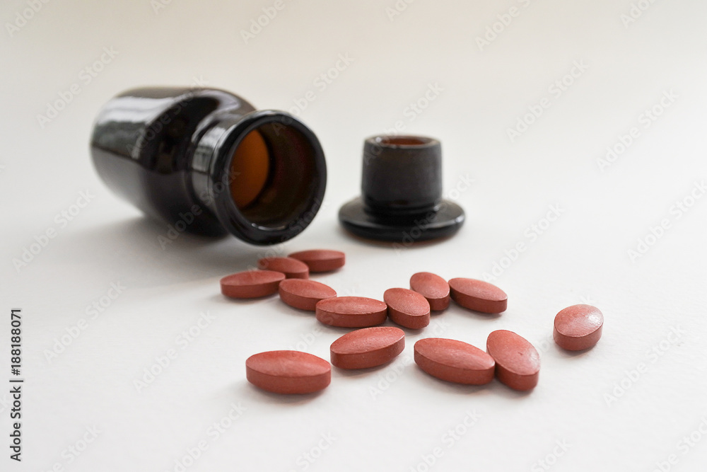 Brown tablets and opaque bottles on white background. Some medicines should be stored in opaque containers to prevent deterioration. Brown tablets and opaque bottles on white background. Some medicines should be stored in opaque containers to prevent deterioration.