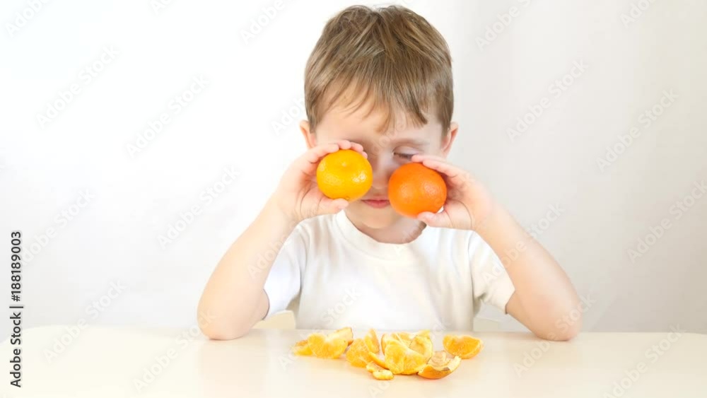 Boy child playing with tangerines. Happy child sitting at table with hands applying tangerines to eyes. Boy child playing with tangerines. Happy child sitting at table with hands applying tangerines to eyes.