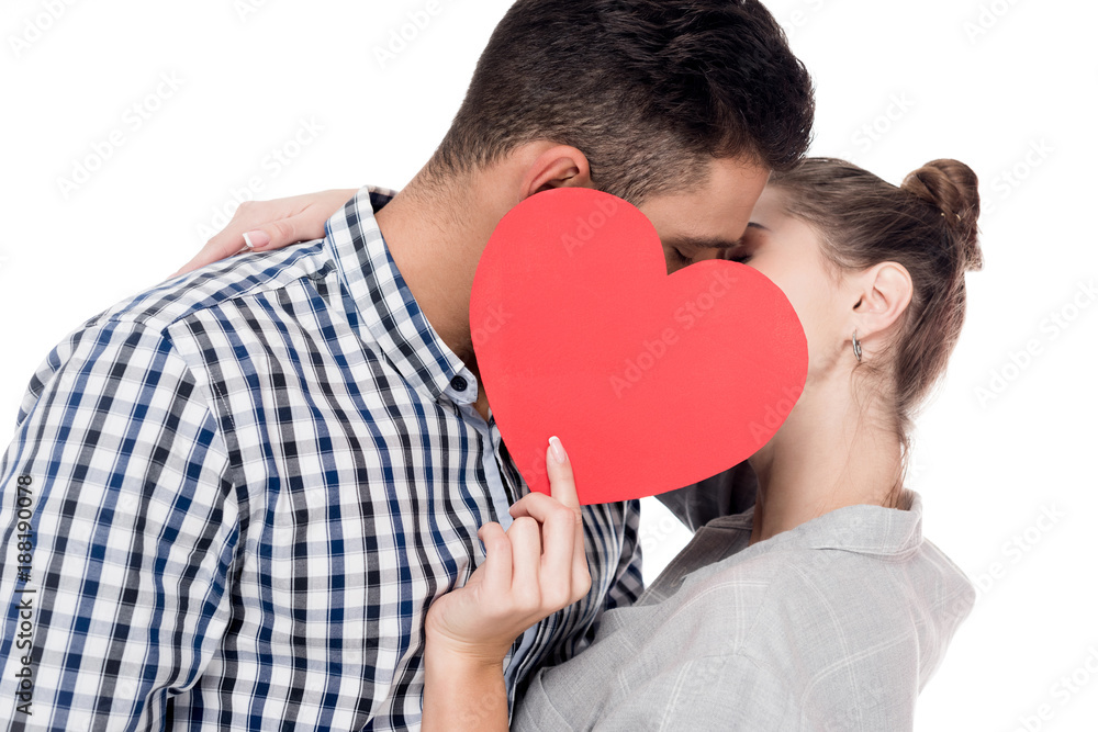 couple kissing and covering faces with paper heart isolated on white, valentines day concept