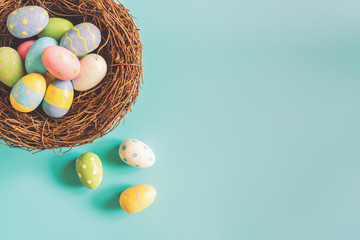 Coloeful easter eggs in nest on pastel color background with space.