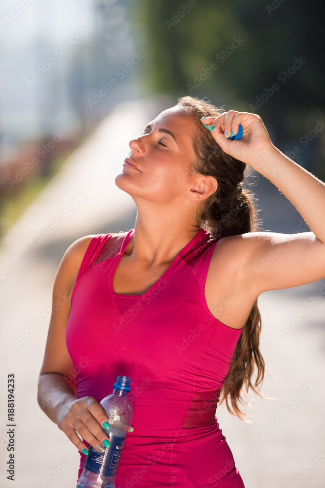 woman drinking water from a bottle after jogging