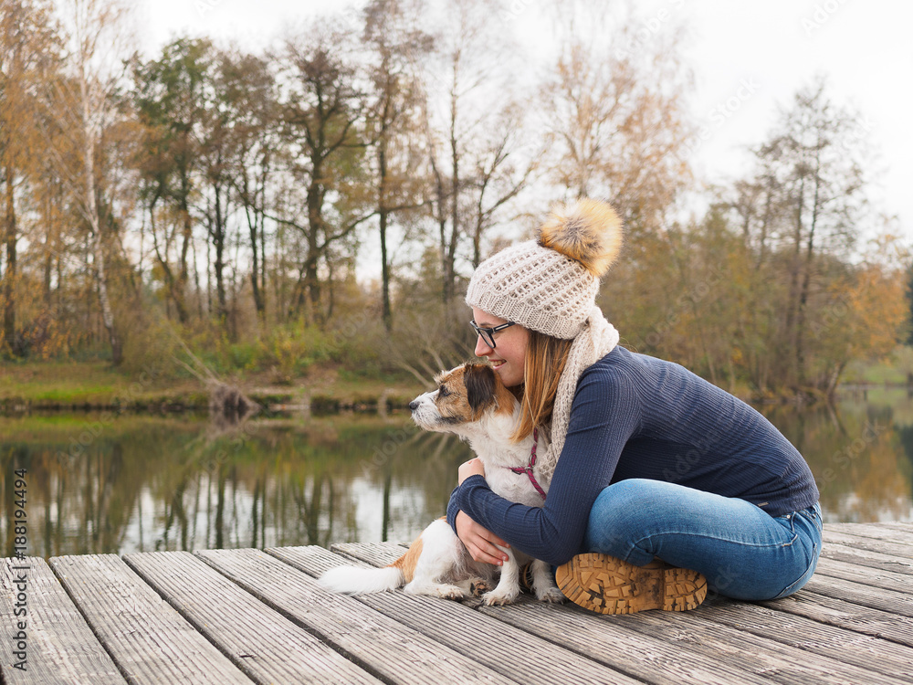 Fototapeta premium Junges Mädchen mit Hund auf einem Holzsteg am See. Lebensfreude, beste Freunde, Glück, Natur.