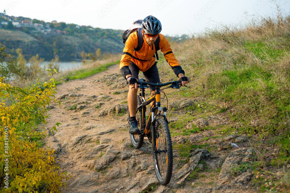 Cyclist in Orange Riding the Mountain Bike on the Autumn Rocky Trail. Extreme Sport and Enduro Biking Concept.
