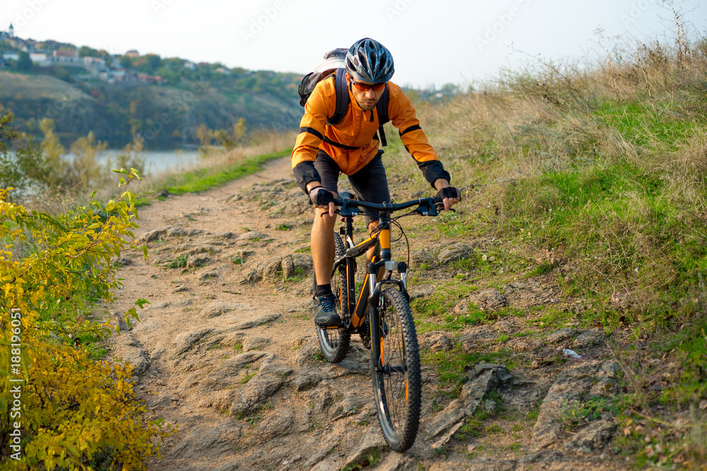 Cyclist in Orange Riding the Mountain Bike on the Autumn Rocky Trail. Extreme Sport and Enduro Biking Concept. Cyclist in Orange Riding the Mountain Bike on the Autumn Rocky Trail. Extreme Sport and Enduro Biking Concept.