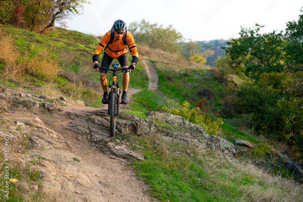 Cyclist in Orange Riding the Mountain Bike on the Autumn Rocky Trail. Extreme Sport and Enduro Biking Concept. Cyclist in Orange Riding the Mountain Bike on the Autumn Rocky Trail. Extreme Sport and Enduro Biking Concept.