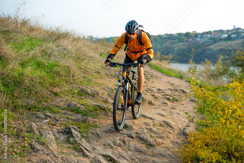 Cyclist in Orange Riding the Mountain Bike on the Autumn Rocky Trail. Extreme Sport and Enduro Biking Concept.