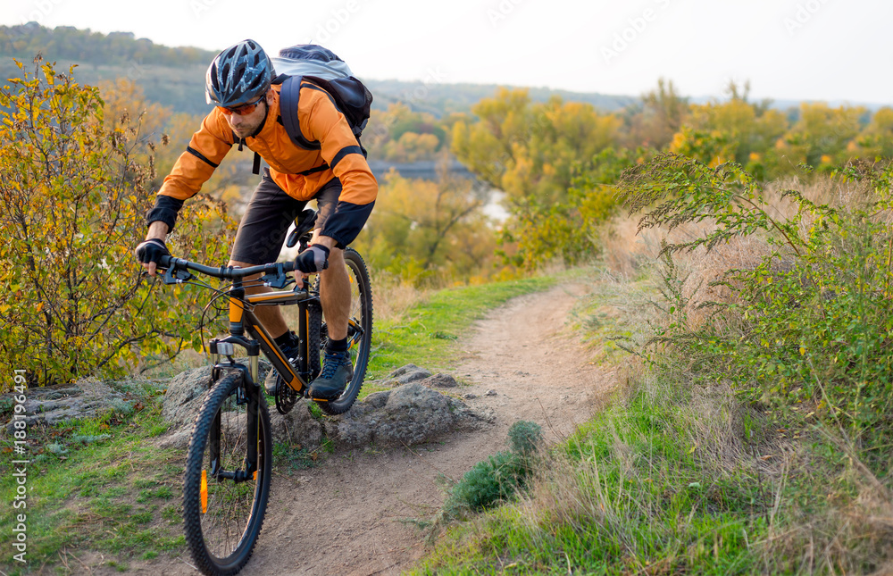 Cyclist in Orange Riding the Mountain Bike on the Autumn Rocky Trail. Extreme Sport and Enduro Biking Concept. Cyclist in Orange Riding the Mountain Bike on the Autumn Rocky Trail. Extreme Sport and Enduro Biking Concept.