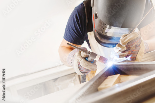 Male in face mask welds with argon-arc welding