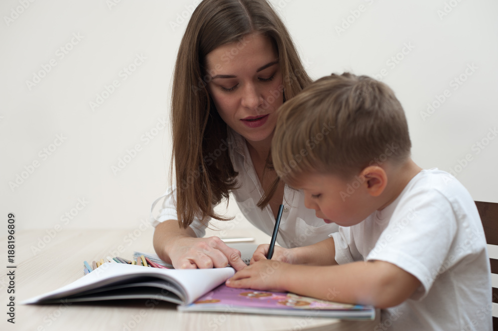 Happy mother is studying with her young child sitting at the table at home Happy mother is studying with her young child sitting at the table at home