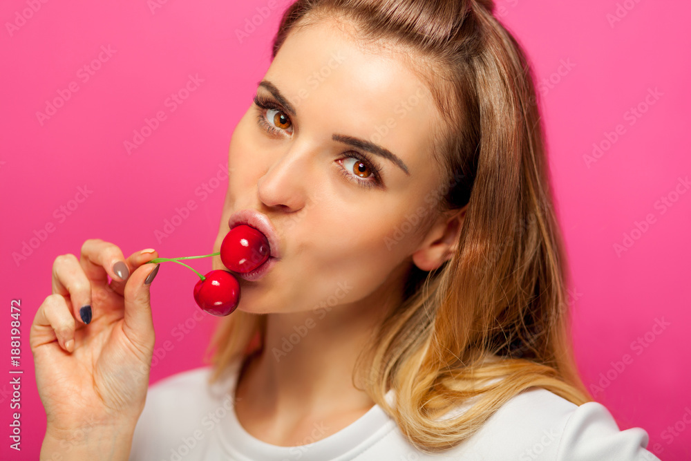 Woman over pink background eating cherry fruit Woman over pink background eating cherry fruit