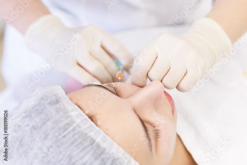 Top view. Close up female face and cosmetologist's hands with syringe during facial beauty injections. Botox pricks, hyaluronic acid injection. Rejuvenation and hydratation. Cosmetology.