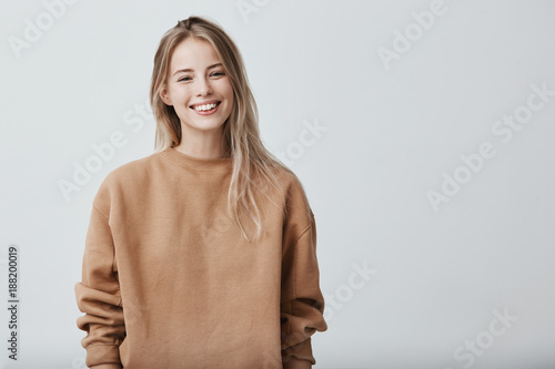 Tela Cheerful positive female youngster with blonde hair, dressed casually, glad to receive graduation congratulations from friends, starting new stage in life
