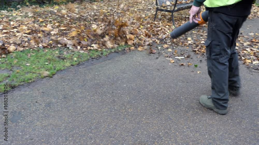 A cleaner cleans the fallen leaves off a sidewalk. A cleaner cleans the fallen leaves off a sidewalk.