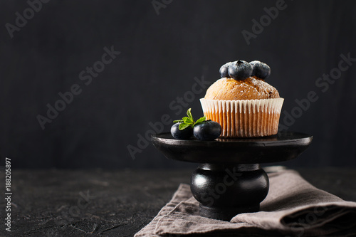 Blueberries muffins or cupcakes with mint leaves on black texture