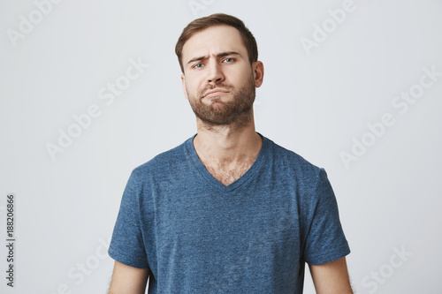 European hesitant bearded man frowns face, thinks over future plans, being little puzzled, poses against gray background. Caucasian male confused and dissatisfied with unexpected news © Cookie Studio