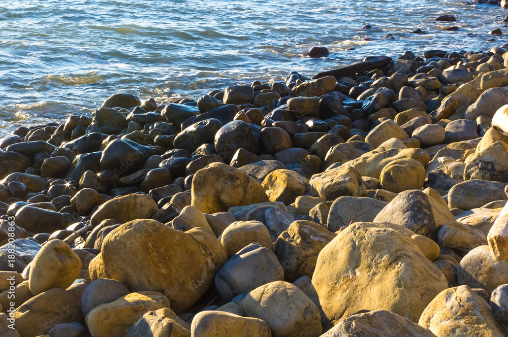Obraz premium rocky sea shore with pebble beach, waves with foam