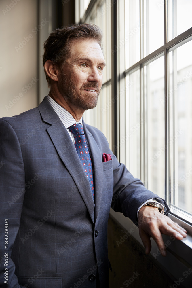 Fototapeta premium Senior white businessman looking out of window, vertical