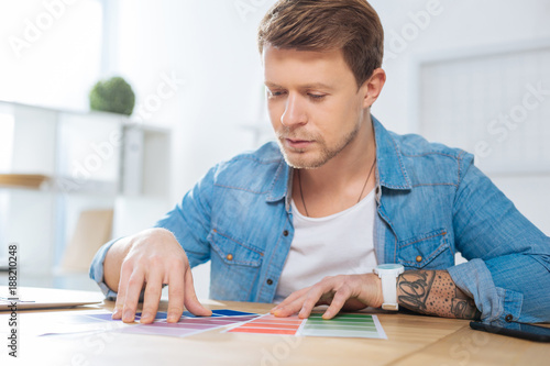 Combining colors. Creative serious busy designer looking concentrated while sitting at the table and working with color palettes