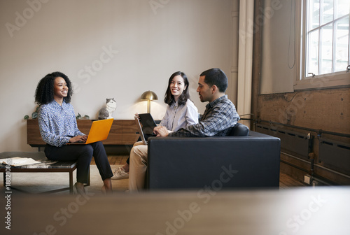 Smiling work colleagues using laptops at a casual meeting