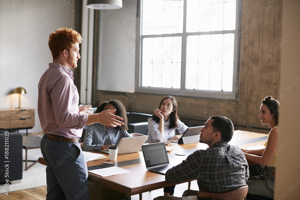 Young man standing to address colleagues at a work meeting Young man standing to address colleagues at a work meeting