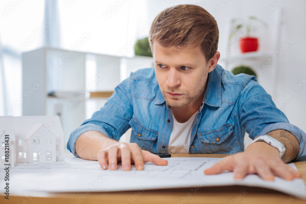 Important decision. Smart responsible experienced engineer sitting at the table and touching the detailed scheme while thinking and looking into the distance Important decision. Smart responsible experienced engineer sitting at the table and touching the detailed scheme while thinking and looking into the distance