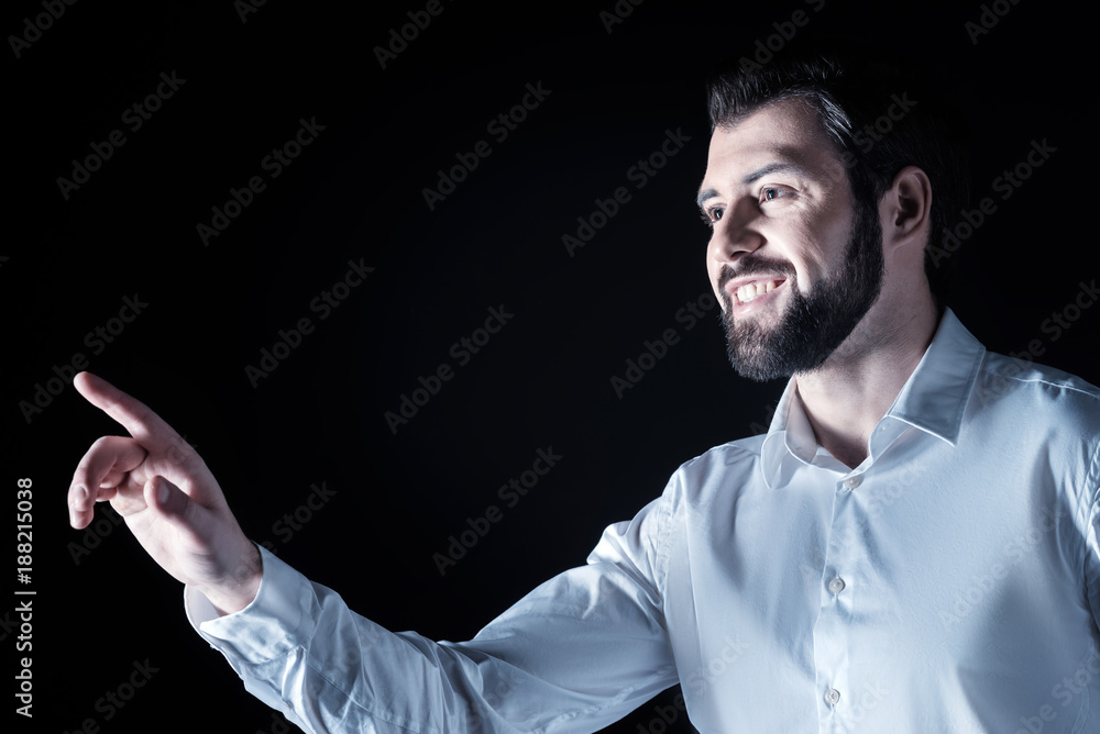 Fototapeta premium Pleasant experience. Joyful nice bearded man smiling and being in a positive mood while working with virtual screen