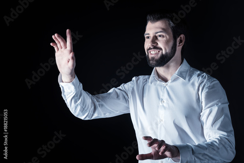 Invisible screen. Happy delighted positive man smiling and using virtual technology while standing against black background