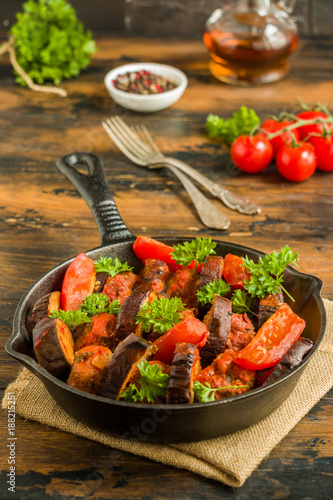 Black cast-iron skillet with Turkish kebab cooked with eggplant and tomatoes on rustic wooden table.