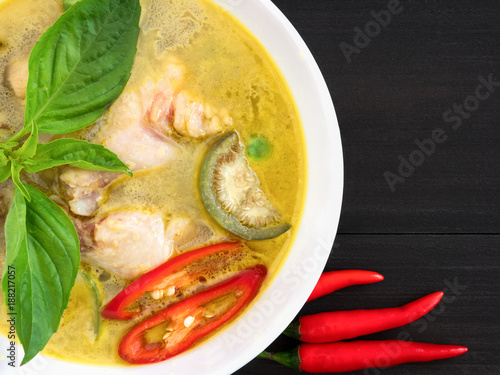 Chicken green curry in white bowl, a traditional Thai cuisine that is spicy sweet curry with cheken meat, egg plant sweet basil and coconut milk, flat lay on black wooden table photo