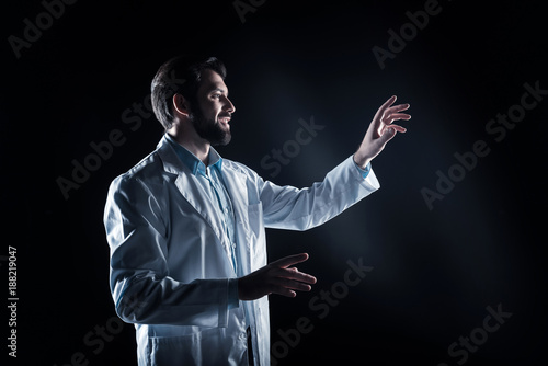 Lab worker. Delighted positive bearded man wearing a labcoart and using modern technology while working in the lab