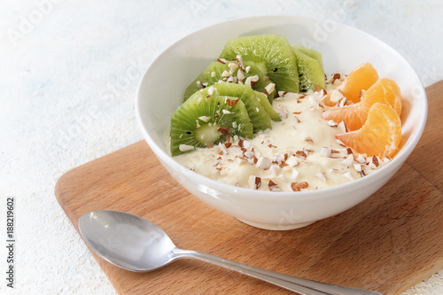 healthy meal with protein from quark or curd cheese, linseed oil with omega 3 fatty acids,  fruits and nuts, budwig diet in a white bowl on a kitchen board and a light background, copy space photo