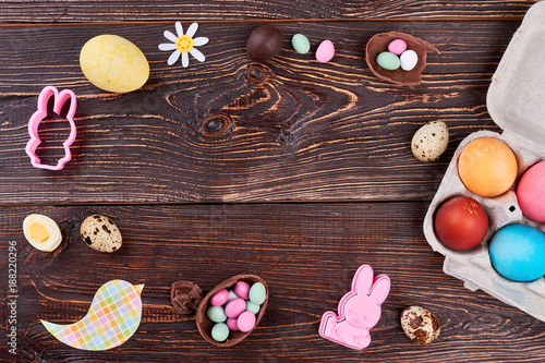 Fototapeta Naklejka Na Ścianę i Meble -  Easter composition on wooden background. Frame from sweets, quail and chicken eggs, rabbit molds, paper cutouts on brown wooden table. Easter handmade decor.