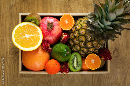 Healthy food in wooden tray   pineapple  orange  tangerine  kiwi  pomegranate and grapefruit on wooden background. Flat lay. Top view