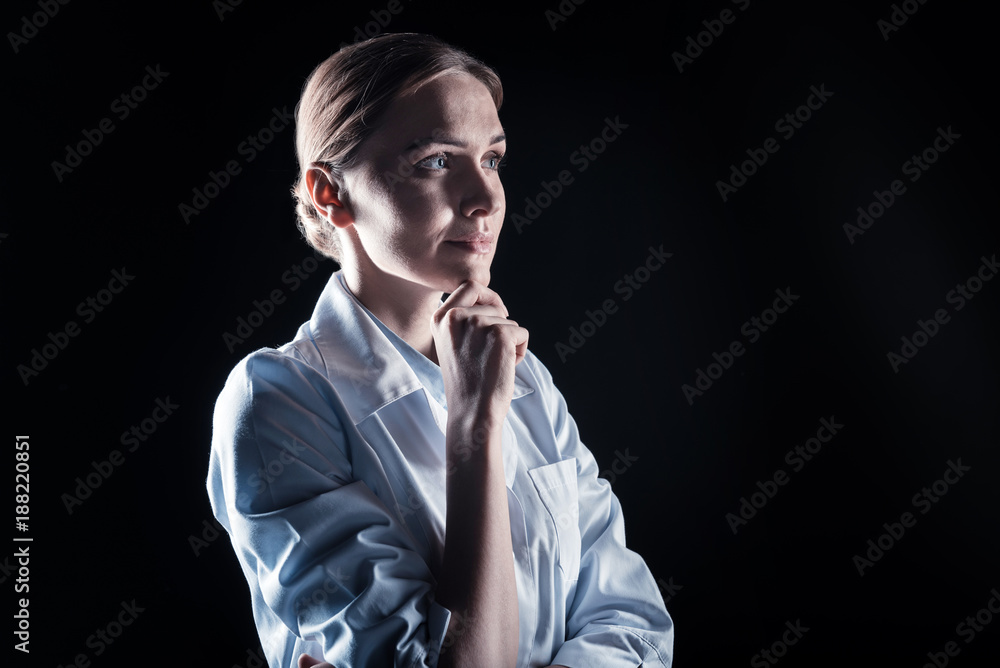 Thoughtful look. Smart nice thoughtful woman holding her chin and thinking while standing against black background Thoughtful look. Smart nice thoughtful woman holding her chin and thinking while standing against black background