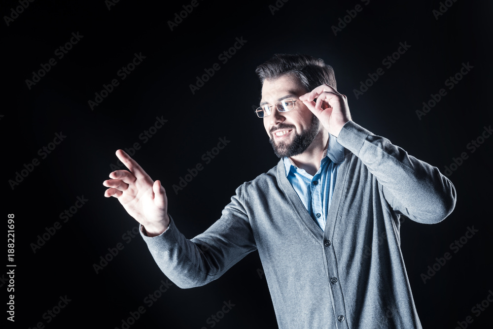 So interesting. Positive joyful smart man smiling and fixing his glasses while looking at the transparent screen