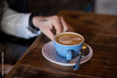 Hipster millennial with hand tattoos gets ready to drink and enjoy fresh and enegretic hot coffee cup  made with organic cow or almond milk and latte art. Early morning routine and caffeine addiction