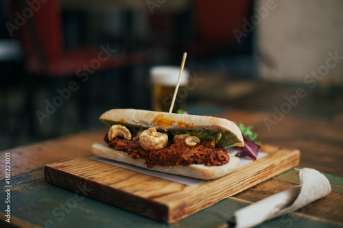 Fatty and savory unhealthy snack, pulled pork sandwich or toast with meat baked and spiced added to it. Served on wooden board with tap beer for lunch photo